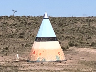 a teepee painted with flowers, prairie grass, and blue sky blends in with the scenery behind it